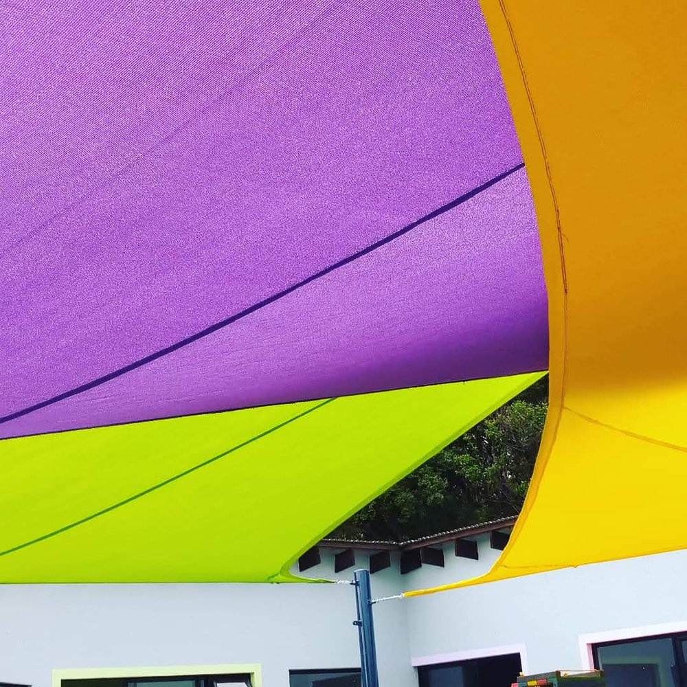 Colourful shade sails in purple, orange and green over a school playground